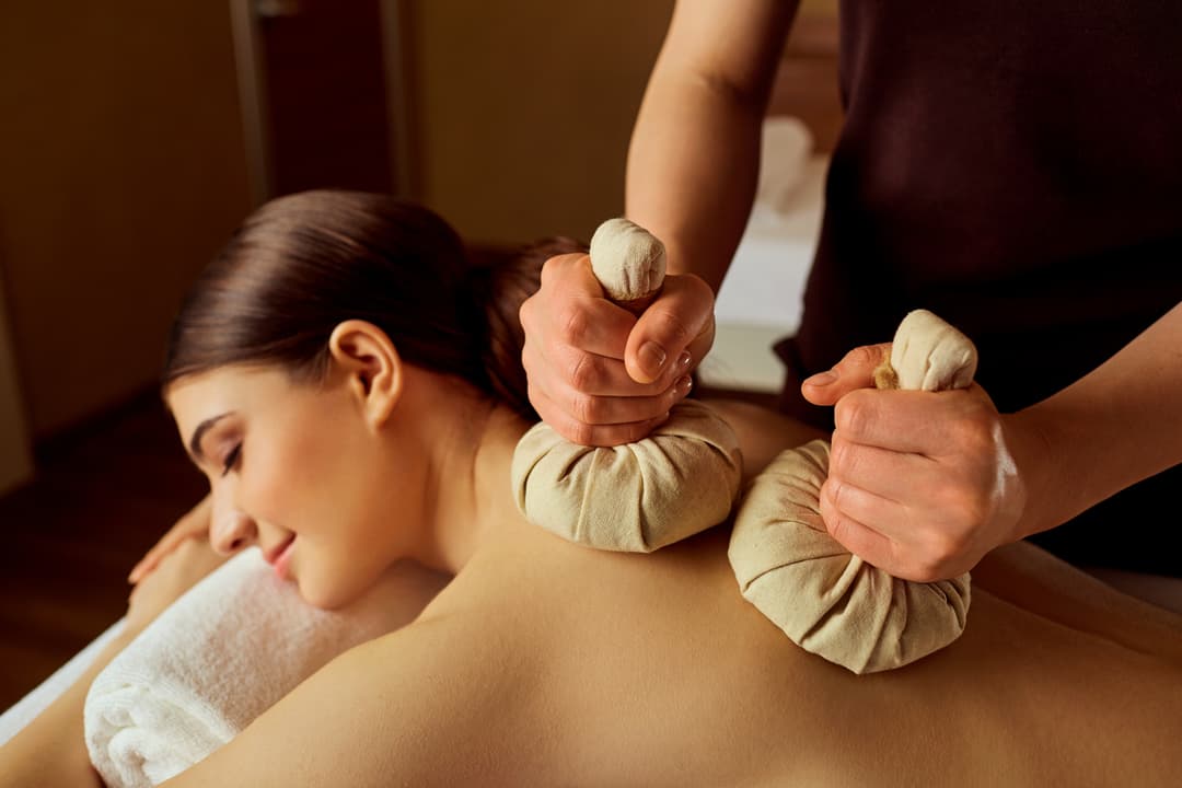 Image of a woman who's relaxed while lying face down and receiving a massage from a female masseuge